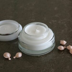 Open jar of luxurious face cream with capsules on a dark textured surface for skincare routines.