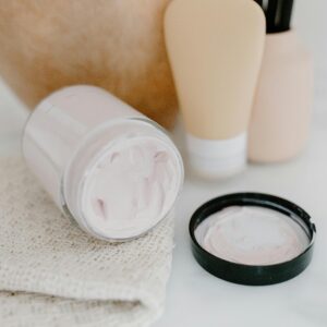 Glass jar with face cream amidst gentle skincare products on a neutral background.