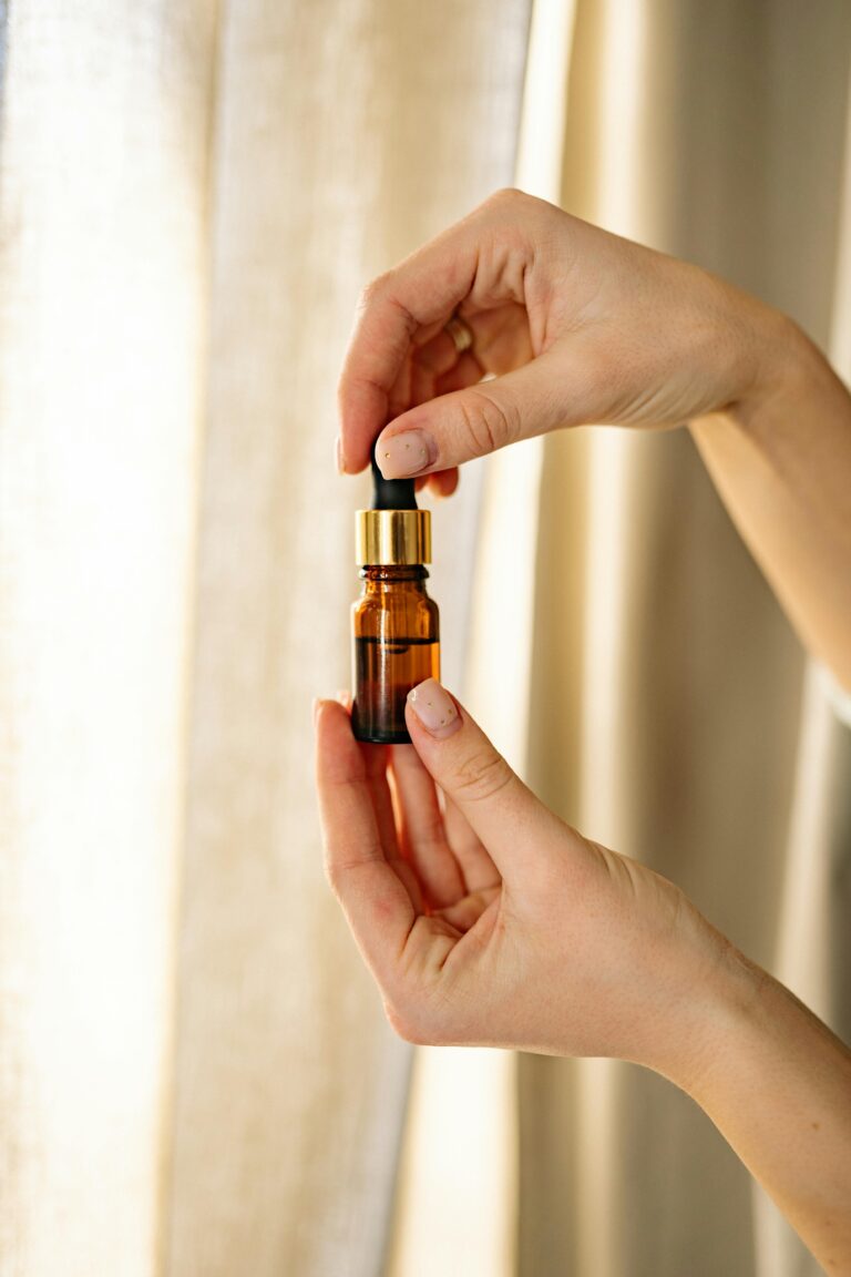 Nosotros Close-up of hands holding an amber essential oil bottle against a soft background.